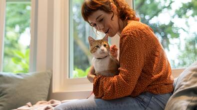 オレンジ色のセーターを着た女性がペットの猫を抱えている